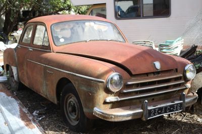 rusted old car parked in front of a trailer in a yard