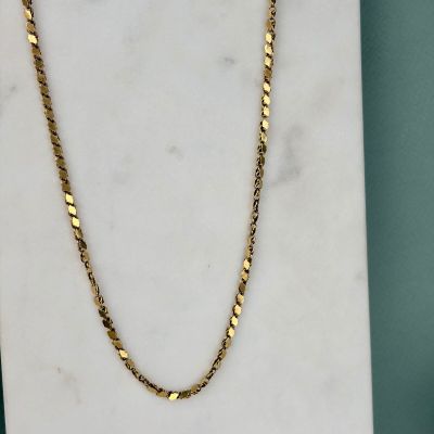 un collier à chaîne en or posé sur une dalle de marbre