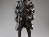 une vieille statue en bronze représentant un homme coiffé d'un chapeau et muni d'une canne