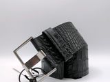 La ceinture est en cuir d'alligator noir et est dotée d'une boucle argentée.