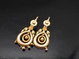 un gros plan sur une paire de boucles d'oreilles en or posées sur une surface noire