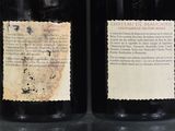 two bottles of wine with labels on them sitting on a table