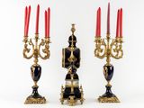 three black and gold candelabs with red candles on them