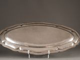 an oval silver platter on a stand on a gray surface