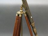 an antique brass telescope on a wooden tripod stand on a gray background