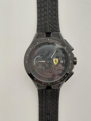 La montre est noire et est munie d'un bracelet noir qui entoure le poignet.