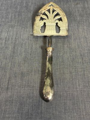 une cuillère en argent avec un manche, posée sur un tissu gris