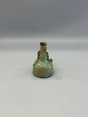 un petit vase vert posé sur une surface blanche