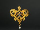 a close up of a gold broochle with a pearl in it