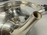 a silver tea pot with a handle on a table