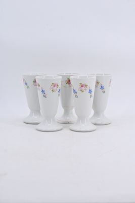 four white cups with floral designs are lined up on a white surface