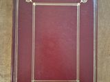 an old red book with gold trim sitting on a wooden table