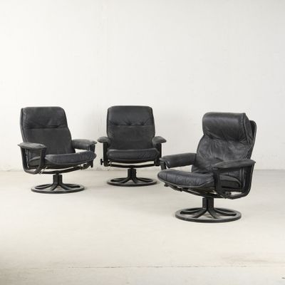 trois fauteuils inclinables en cuir noir et un tabouret dans une pièce blanche