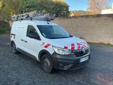 La camionnette blanche est garée sur un parking, avec une échelle posée sur le toit.