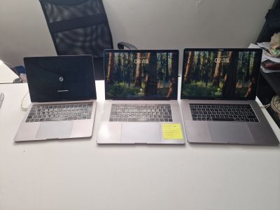 three laptops sitting on a white table with a black chair in the background