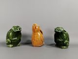 trois figurines en céramique représentant des grenouilles et un oiseau, posées sur un fond gris