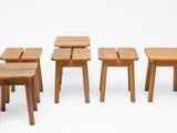 Plusieurs petits tabourets et tables en bois sont alignés en rangée