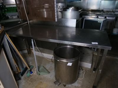 une grande table en inox dans une cuisine, avec une poubelle