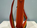 an orange purse with a yellow, red, and yellow strap