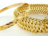 deux bracelets en or posés sur une surface blanche, sur fond blanc