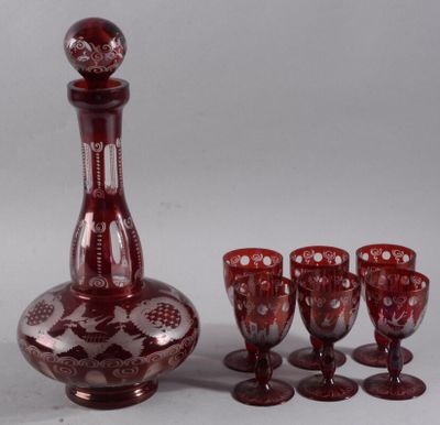 une carafe en verre rouge, avec six verres à vin à côté