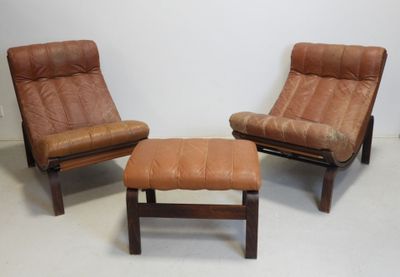 two brown leather chairs and a foot stool in a white room