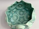 a small green bowl with holes in it on a white surface