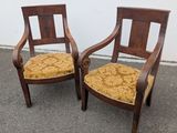 two wooden chairs with yellow upholstered cushions sit in front of a white wall