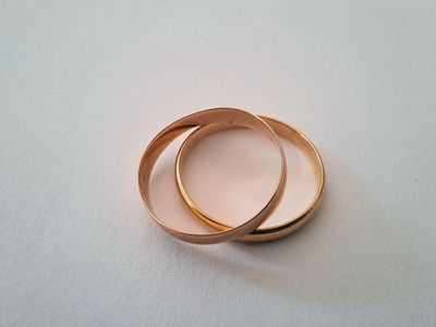 two gold wedding rings on a white surface