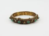 a gold bracelet with green stones on a white background