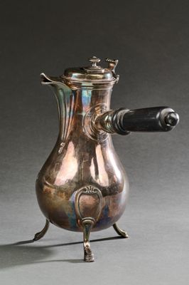 une cafetière en argent avec une poignée noire, posée sur un socle