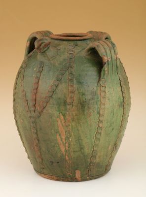 un vase vert muni d'une anse, posé sur une surface blanche