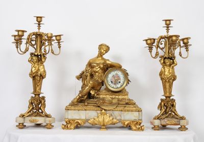a gold clock sitting on top of a table next to three candelabs