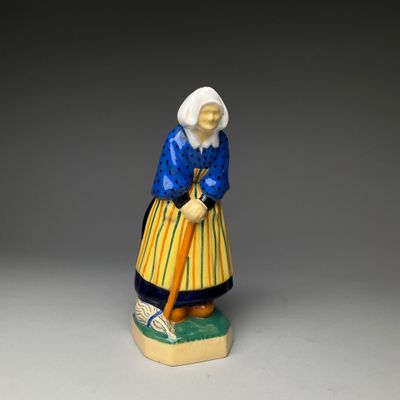 une vieille figurine représentant une femme avec une canne, assise sur une table