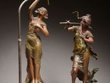 deux statues en bronze représentant une femme et un homme avec un oiseau sur la tête