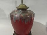 a red vase sitting on a table with a lamp on top of it