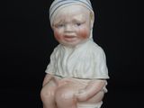 a porcelain figurine of a baby sitting on a toilet