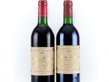 two bottles of red wine sitting next to each other on a white surface