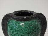 a green vase with a black handle on a white surface