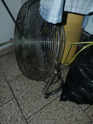 un ventilateur posé par terre à côté d'un sac poubelle