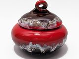 un bol rouge et noir muni d'un couvercle, posé sur une surface blanche