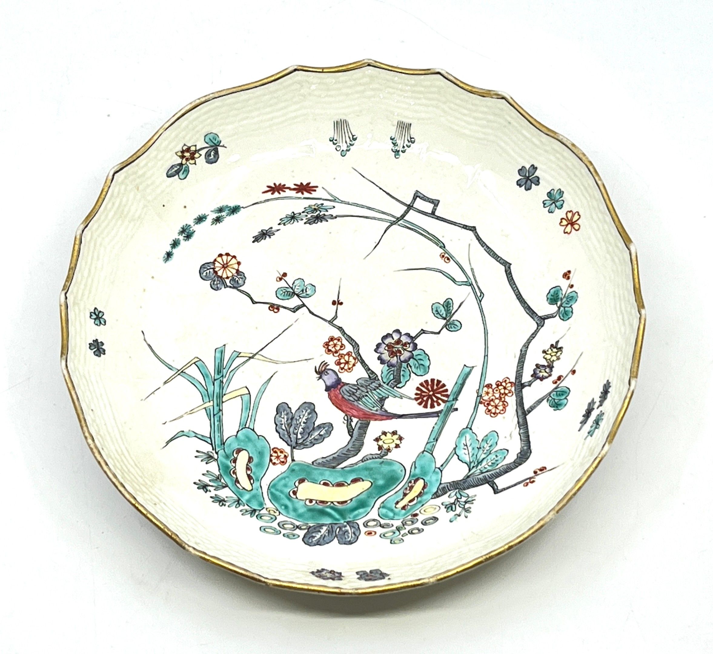 CHANTILLY. Assiette creuse en porcelaine à décor polychrome de style Kakiemon. L'aile à décor en relief à l'imiTation...