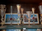 Plusieurs vases en verre et des tableaux sont posés sur une étagère dans un meuble.