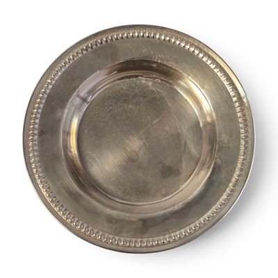 une assiette en argent avec un bord perlé sur un fond blanc