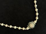 a necklace with pearls and a flower on a black background