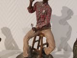three figurines of men sitting on stools in a row