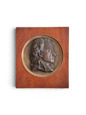 une image représentant un médaillon en bronze à l'effigie d'un homme, monté sur une plaque en bois