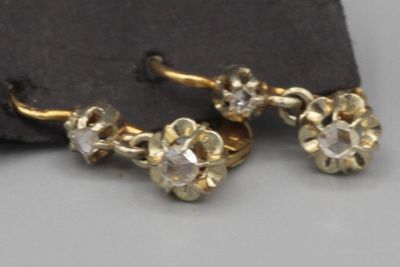 paire de boucles d'oreilles dorées ornées de cristaux transparents, présentées sur un tissu noir