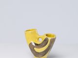 un vase jaune et marron posé sur une table blanche, sur fond gris
