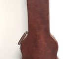 a brown guitar case sitting on the floor next to a white wall